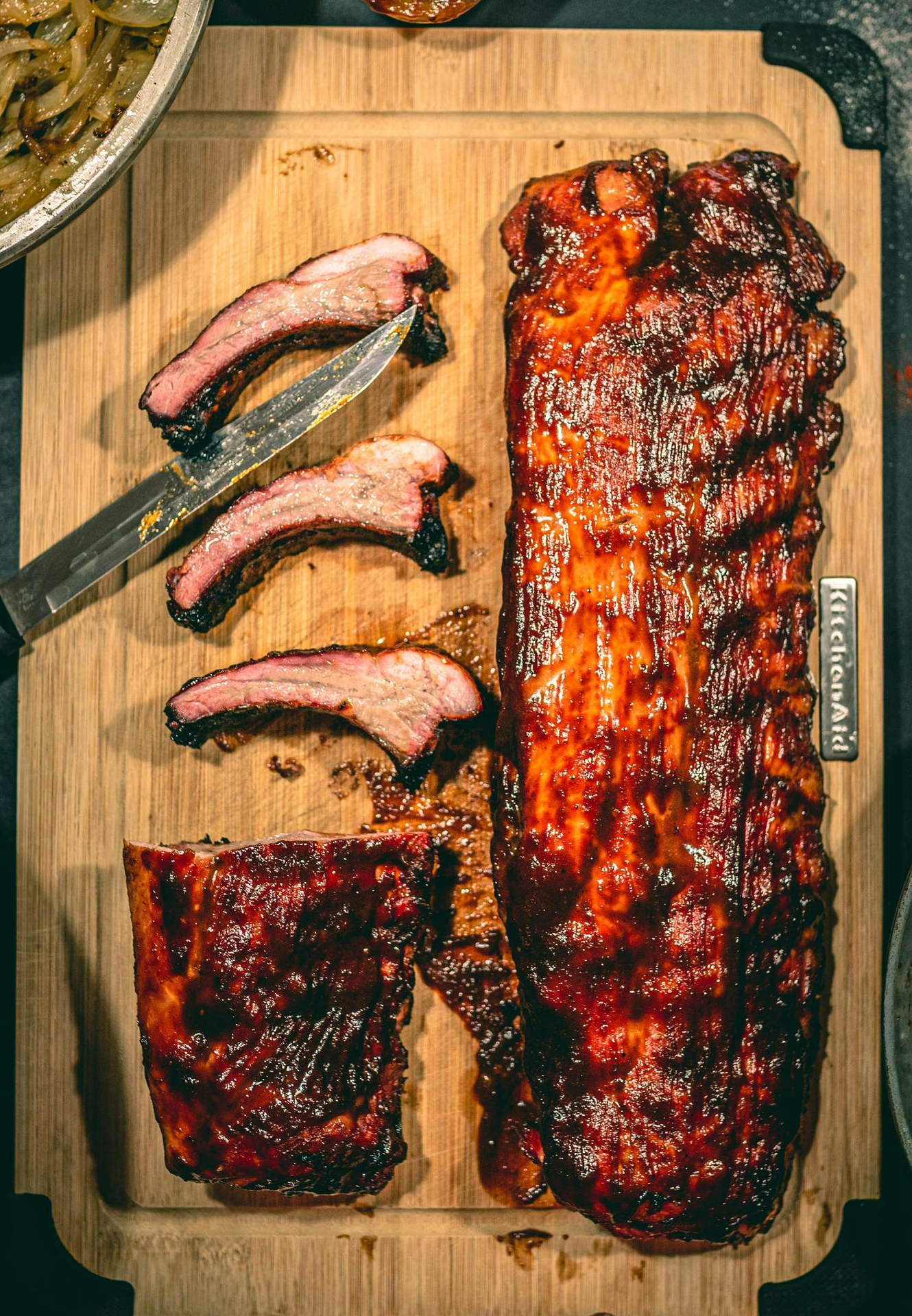 Rack of glazed ribs, some sliced, on a wooden cutting board with a knife.