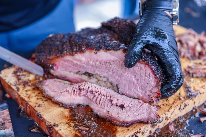 Brisket being sliced on a wooden board, held by a gloved hand.