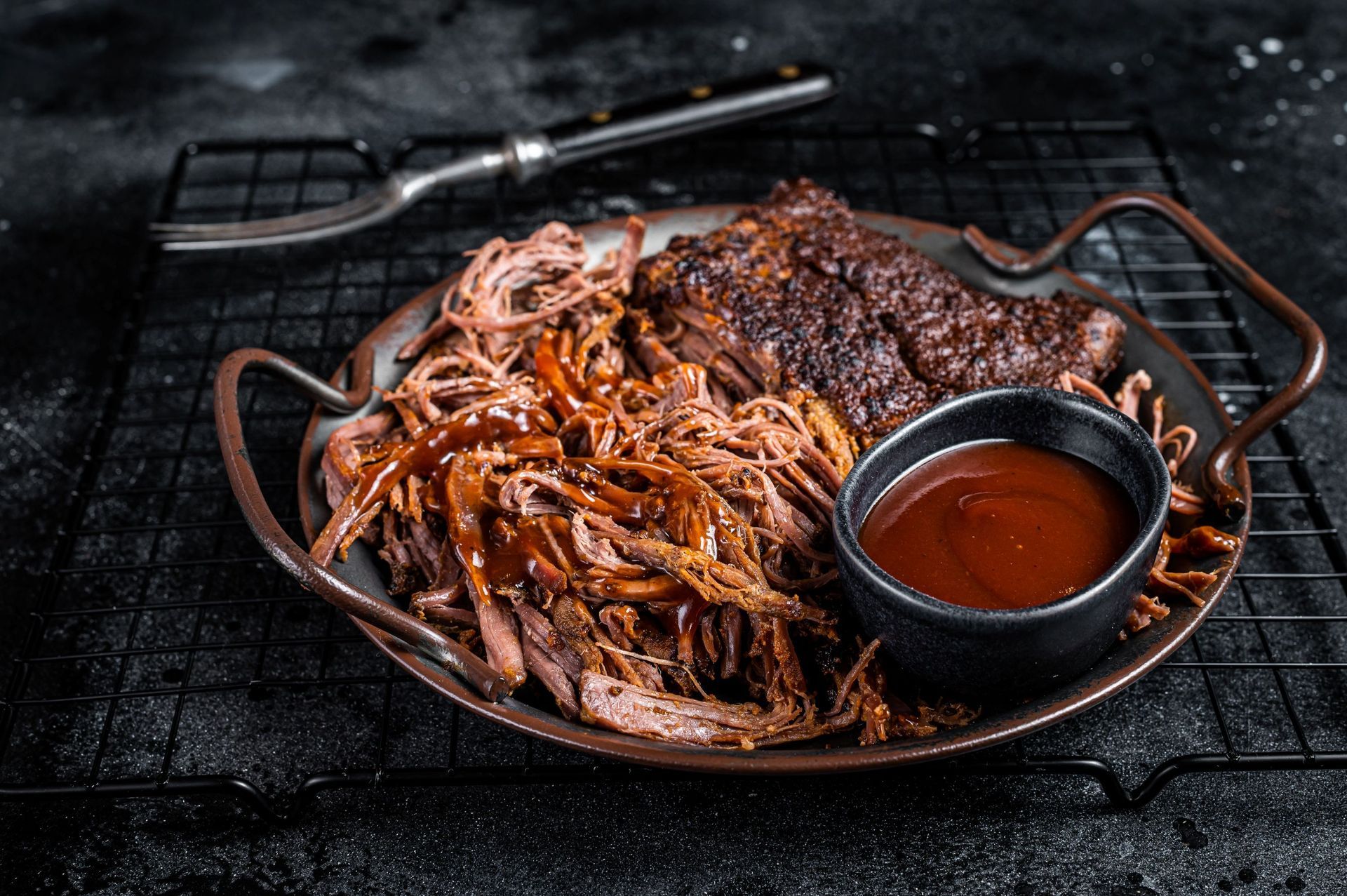 Pulled pork with barbecue sauce in a black bowl on a metal tray.