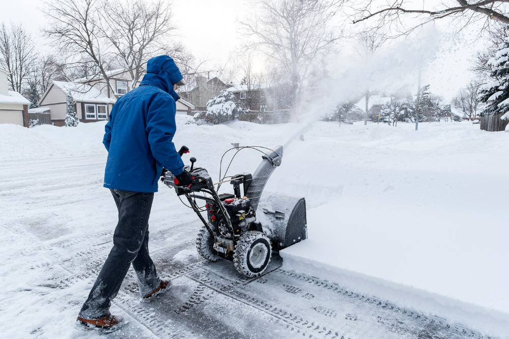 A man is using a snow blower to clear a driveway.