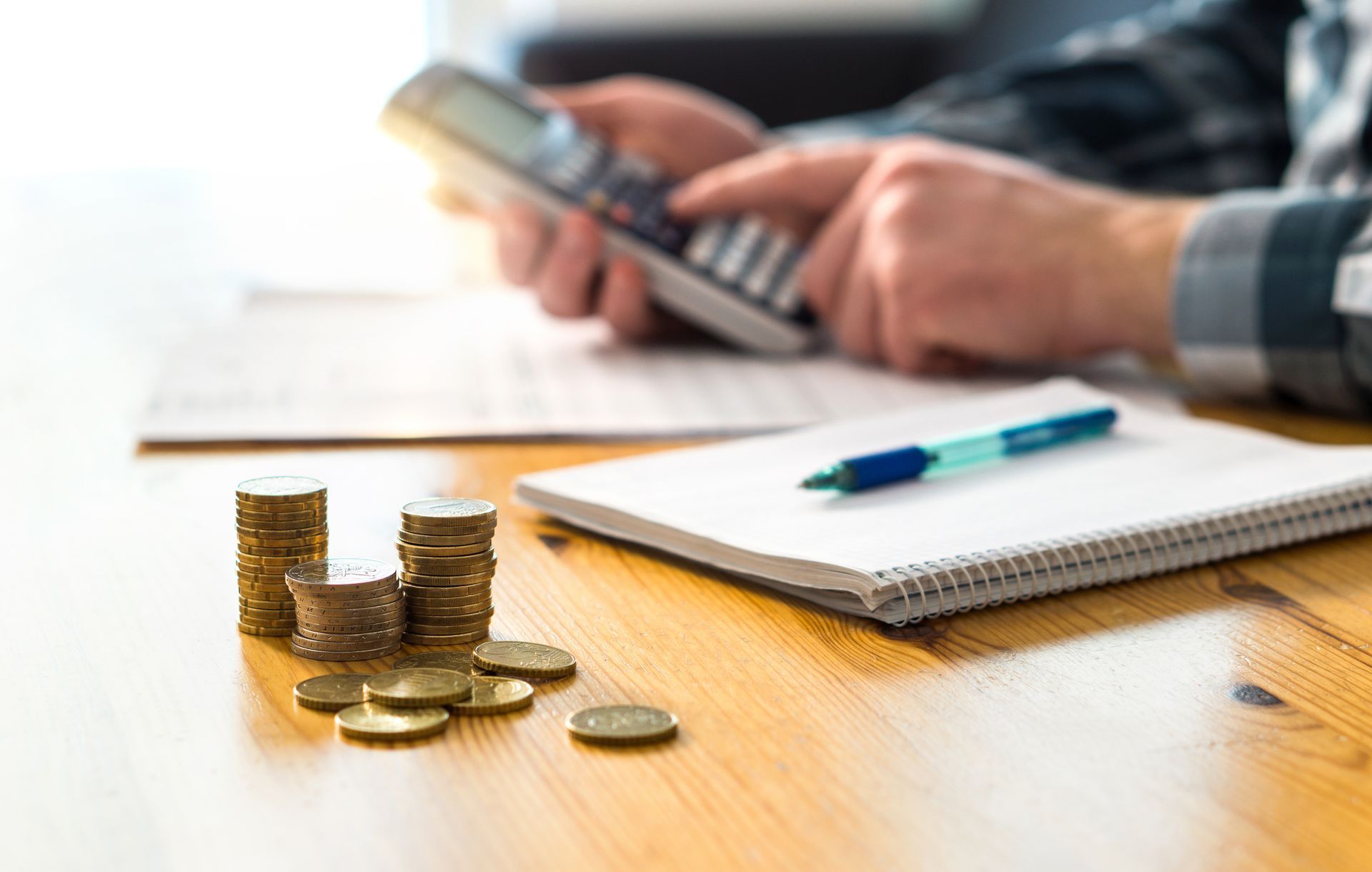 Stacks of coins and person using a calculator at a desk with notebook and pen