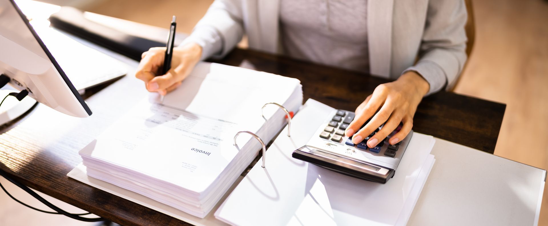 Person working at a desk, writing on documents and using a calculator