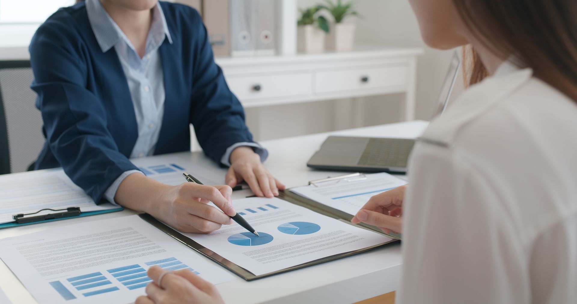 Two women at a desk reviewing charts and graphs, one pointing with a pen