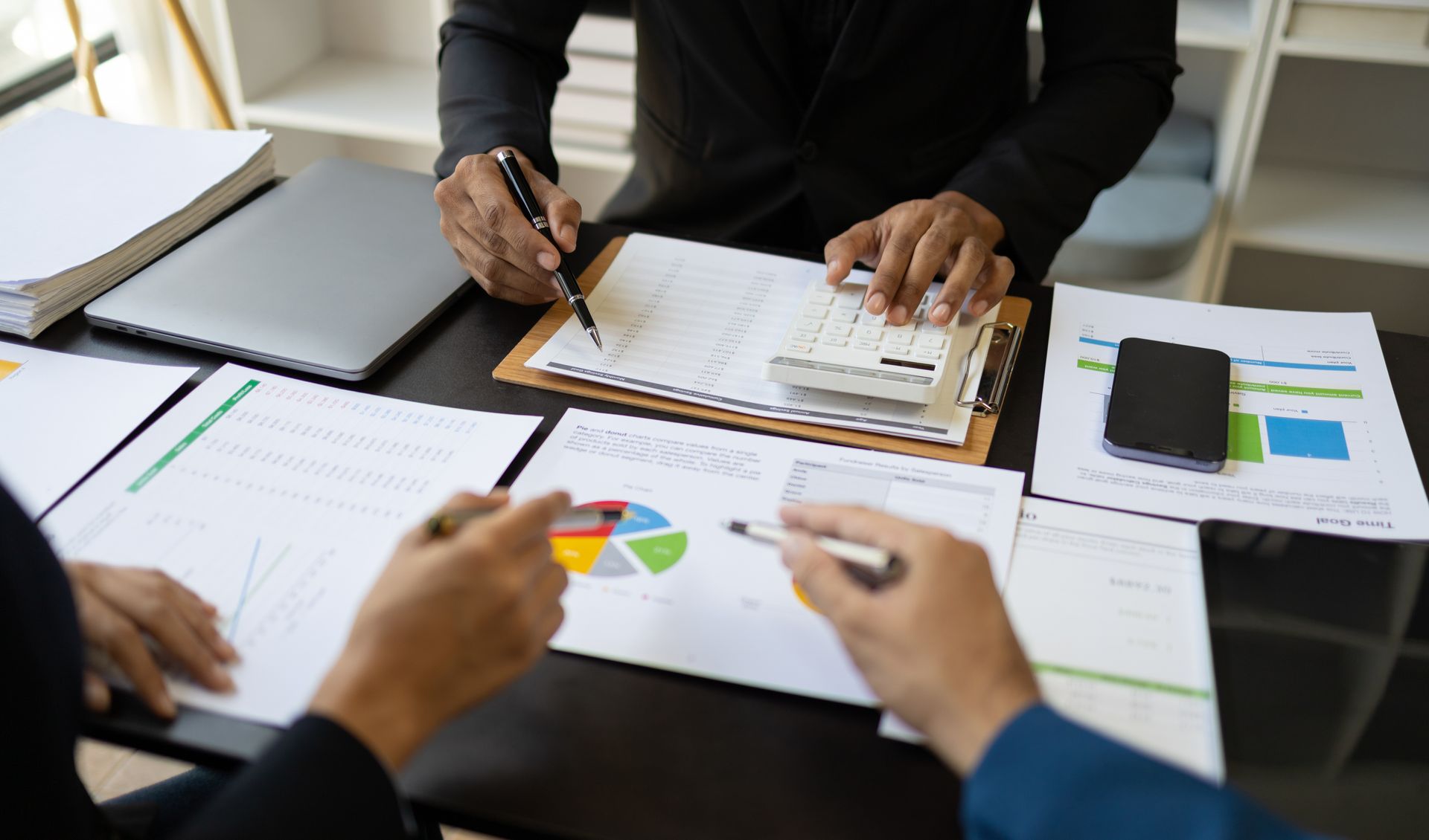 Businesspeople at a table reviewing financial data with charts, calculator, and laptop