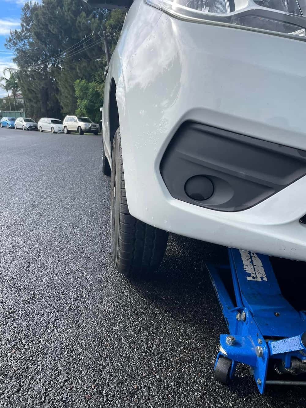 A White Car Is Sitting on A Blue Jack in A Parking Lot — BEB Automotive In Berkeley, NSW
