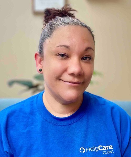 Woman in a blue shirt with the HelpCare Clinic logo, smiling, indoors.