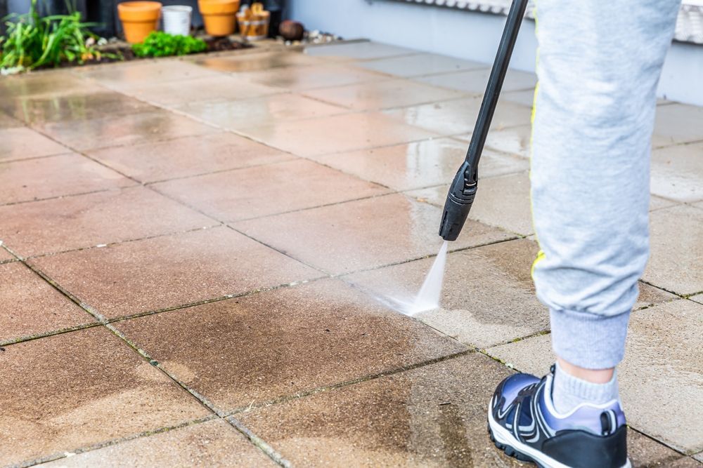A person is cleaning a patio with a high pressure washer.