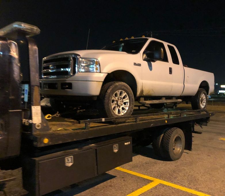 A white truck is sitting on top of a tow truck.