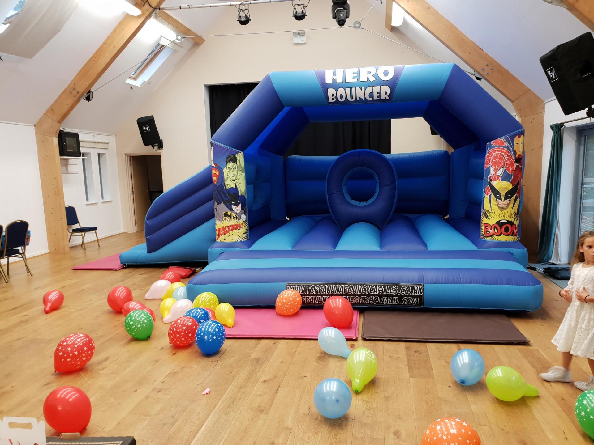 super hero theme slide combo bouncy castle in a village hall