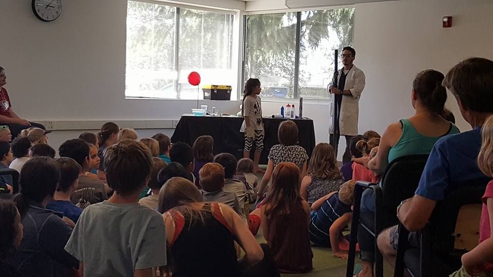A man in a lab coat is giving a presentation to a group of children.