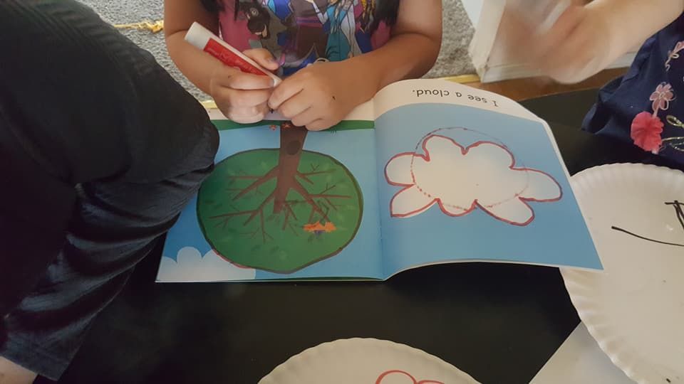 A little girl is drawing a tree and a cloud in a book.