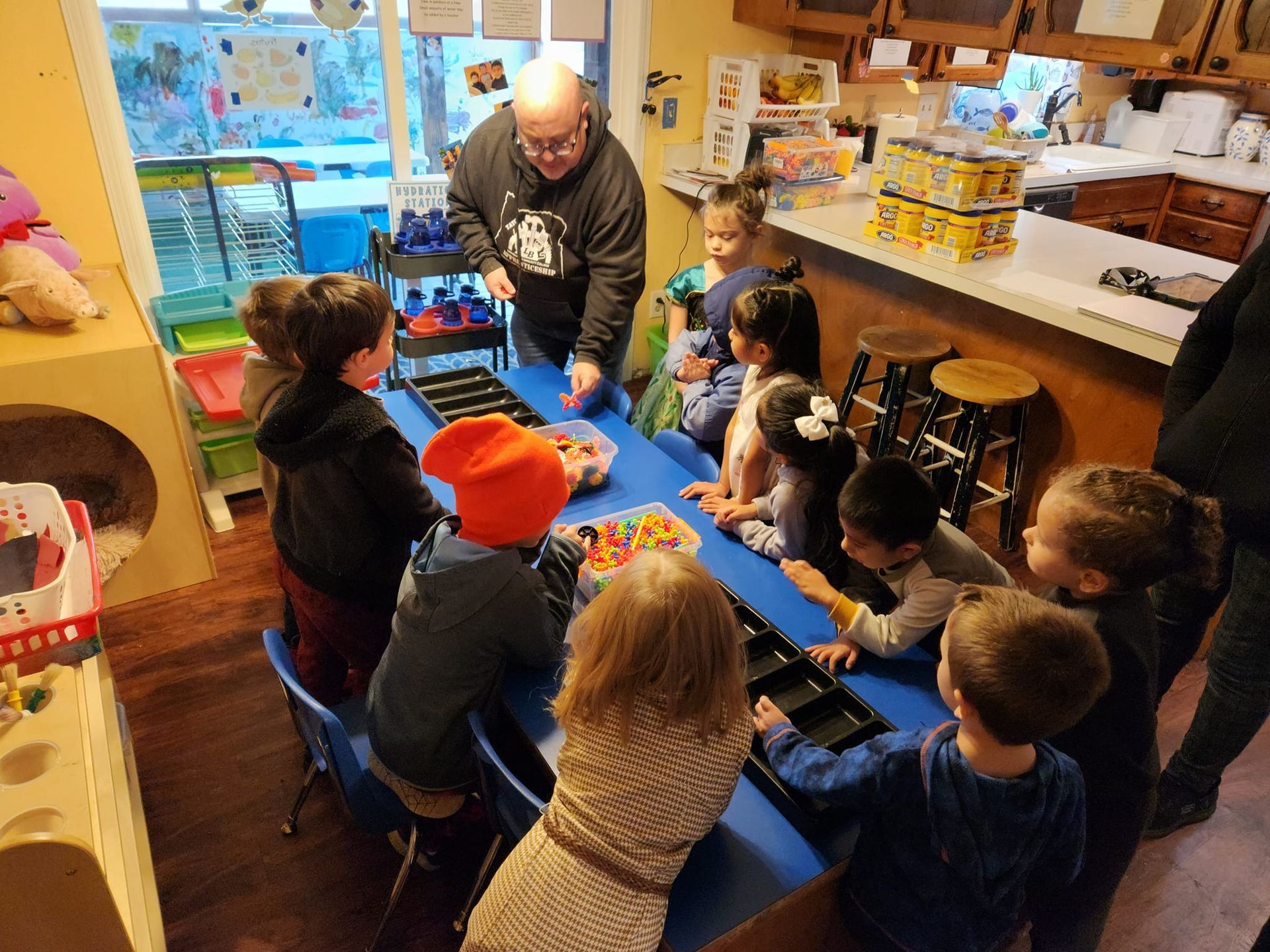A group of children are sitting around a table with a man standing behind them.