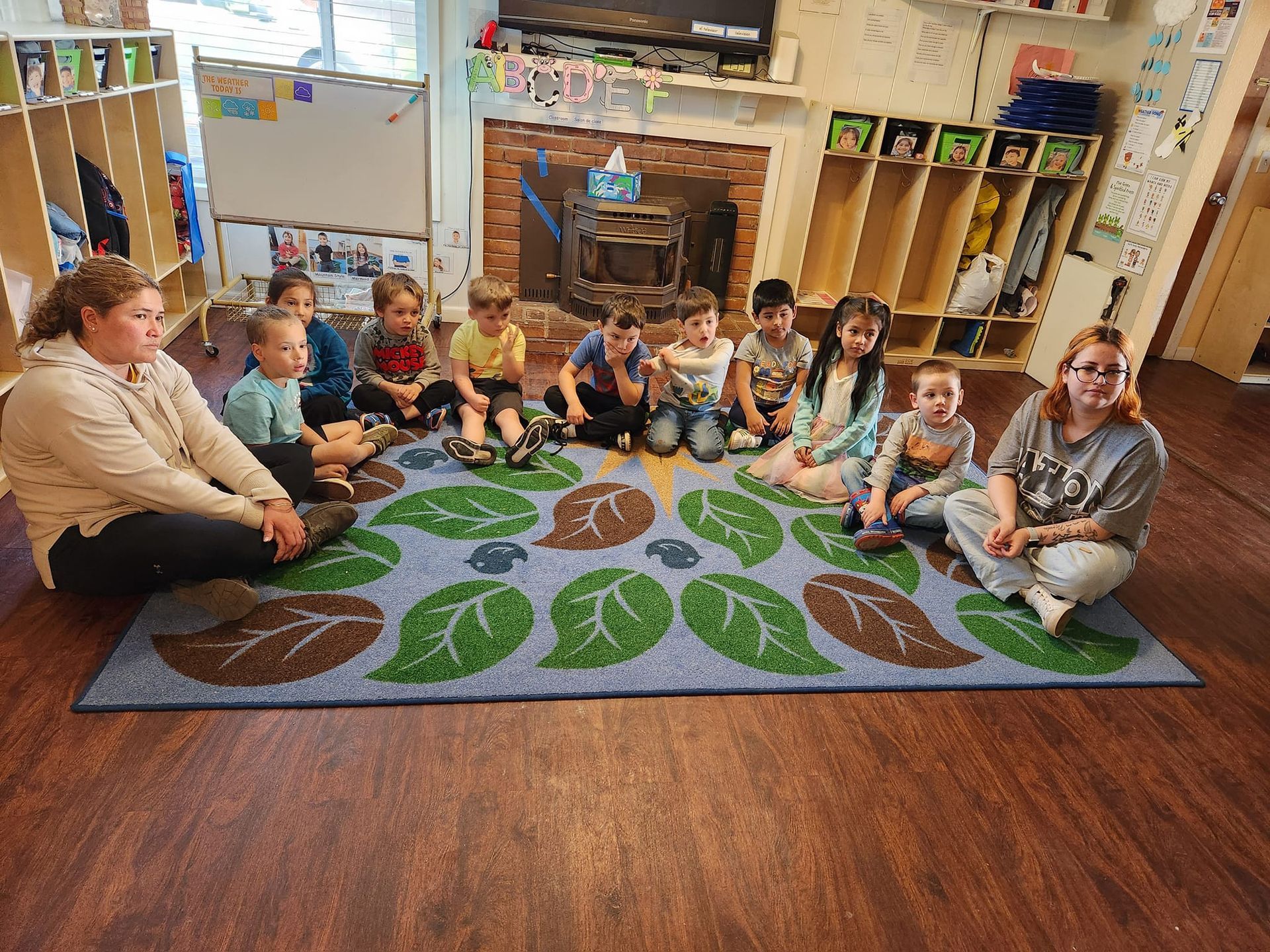 A group of children are sitting on a rug in a classroom.