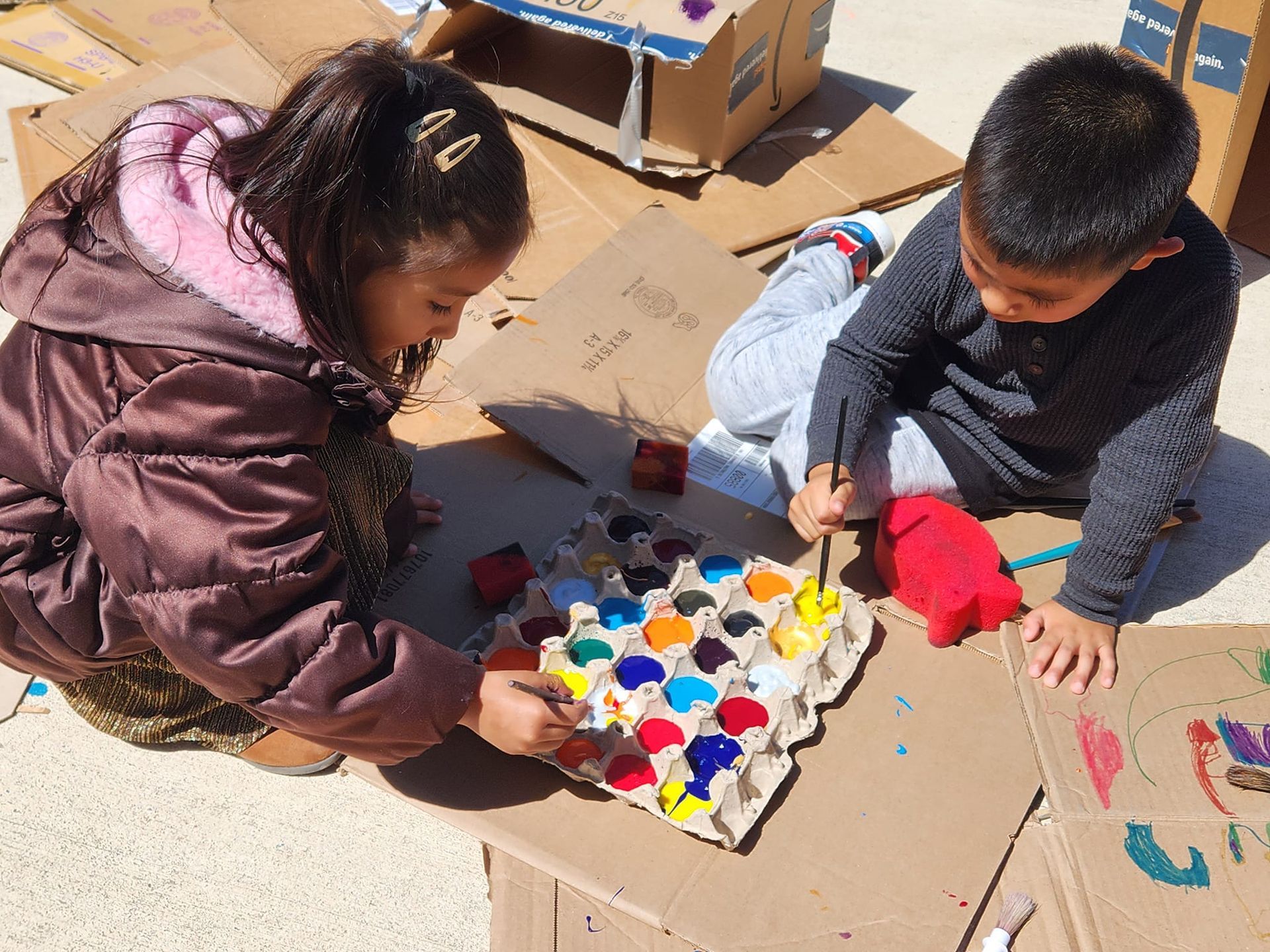A little girl in a purple shirt is standing in front of a pile of cardboard boxes.