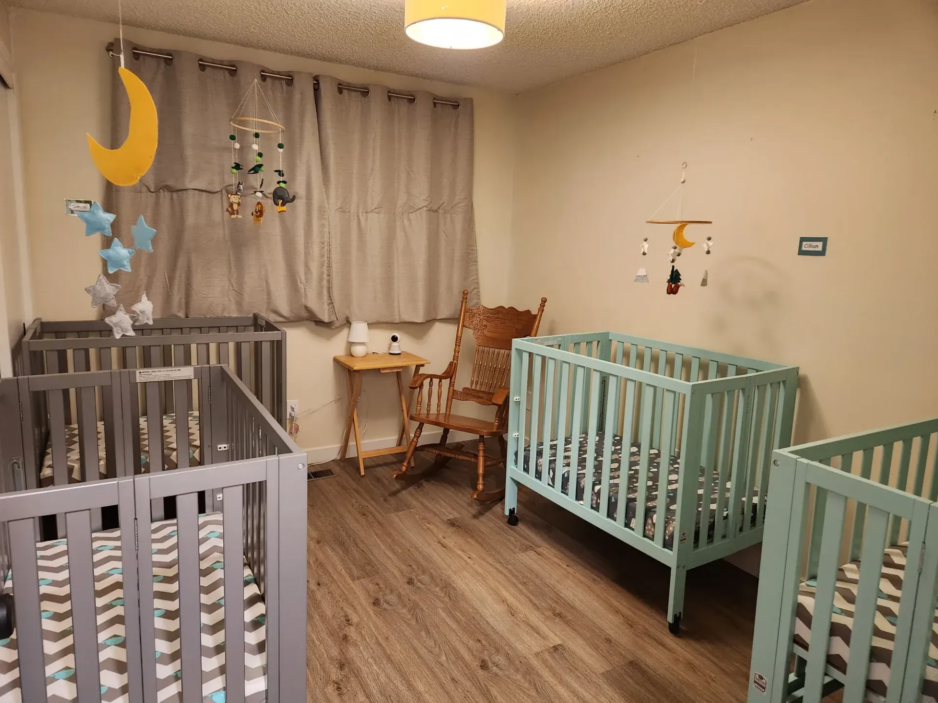 A room with three cribs and a rocking chair.
