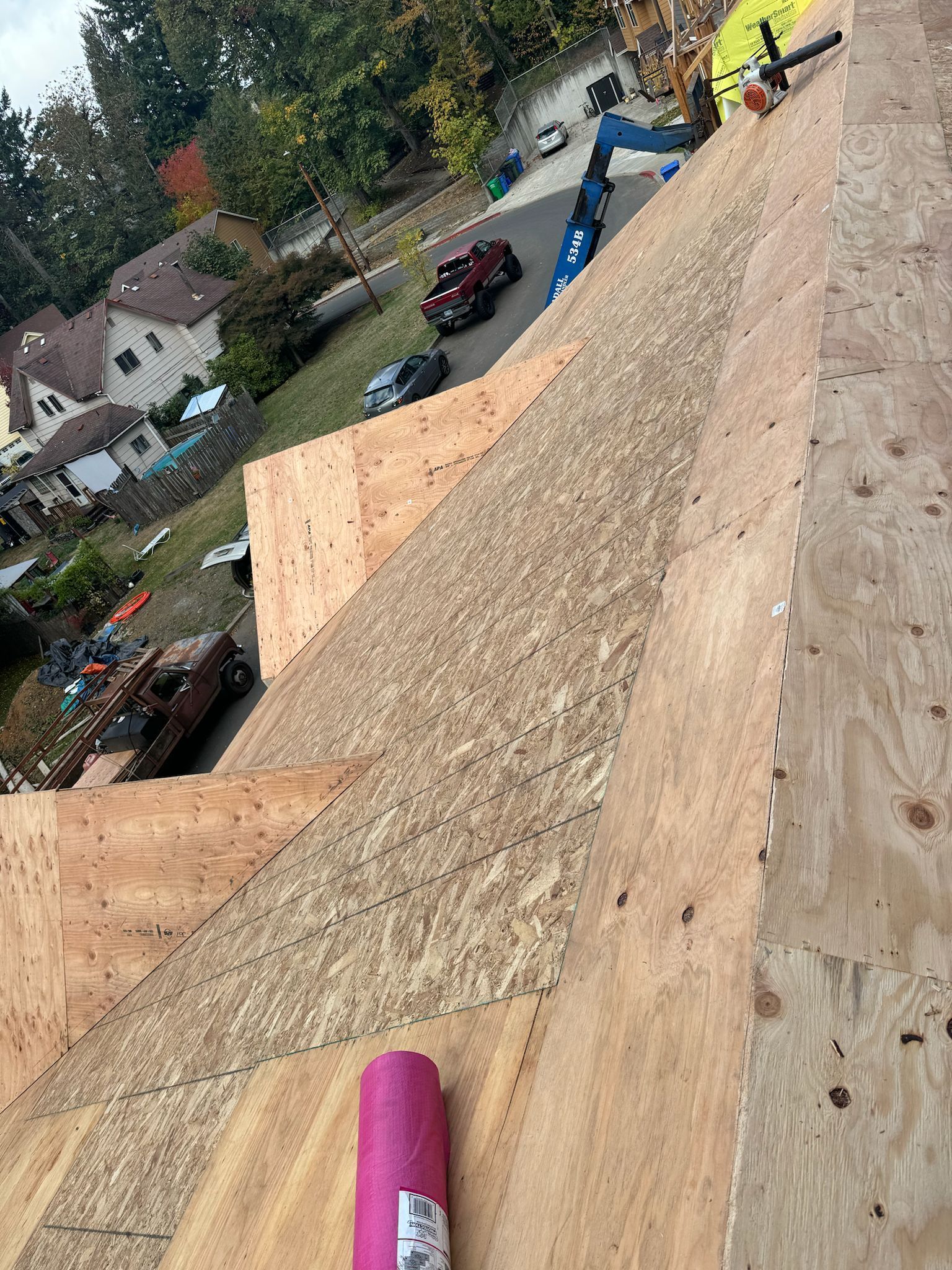 View from a roof, showing plywood sheeting, a pink roll, and neighborhood street below.