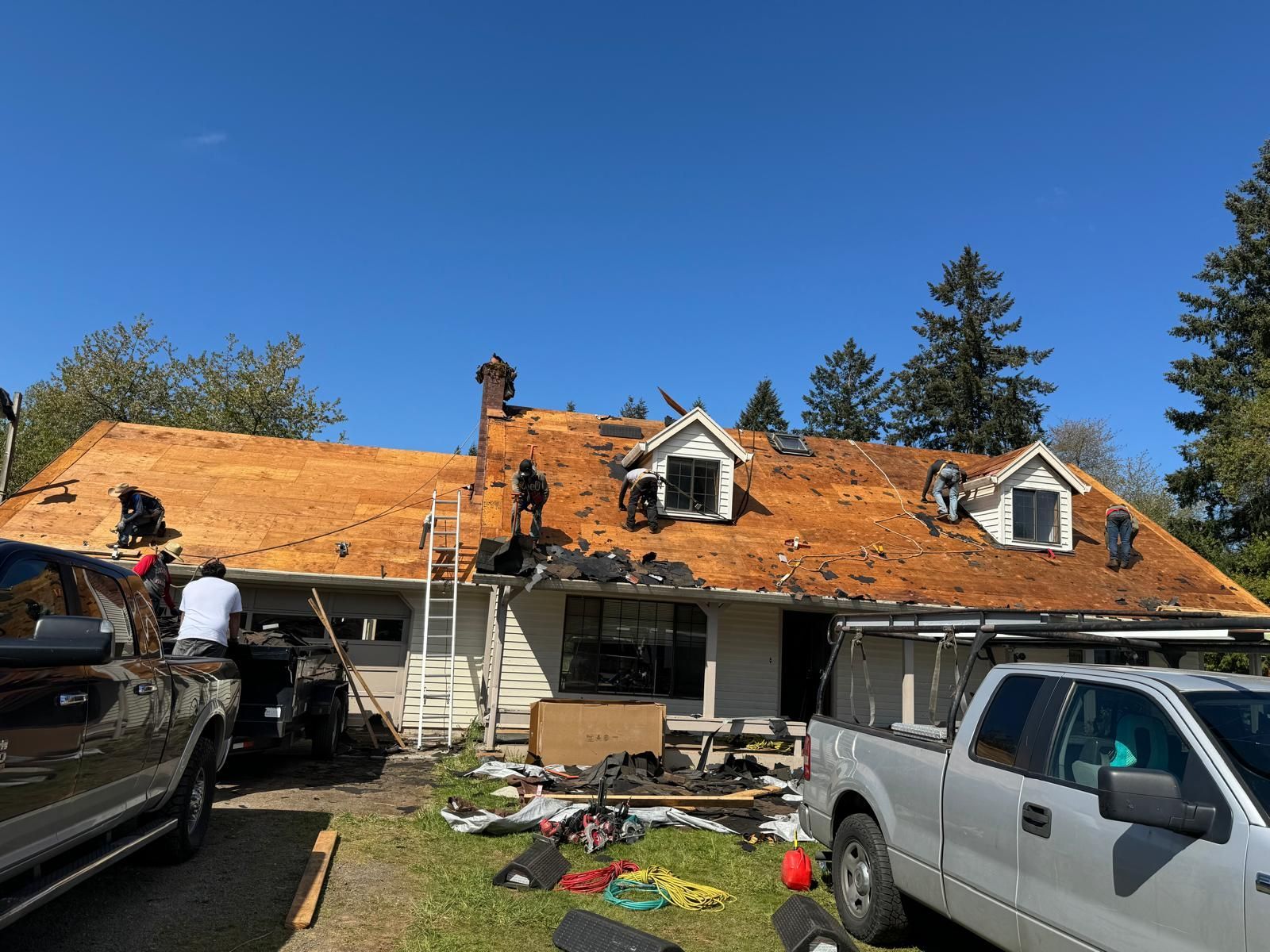 Workers removing roofing materials from a house under a clear, blue sky.