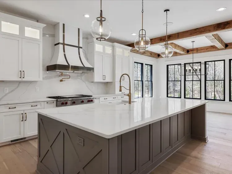 Modern white kitchen with dark island, stainless range hood, and large black-framed windows