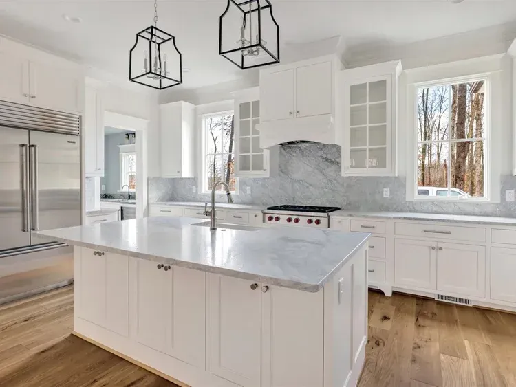 Bright modern white kitchen with marble island, stainless appliances, and large windows