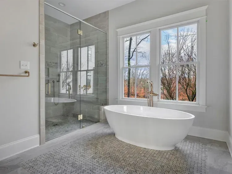 Modern bathroom with glass shower, freestanding tub, and large windows overlooking trees