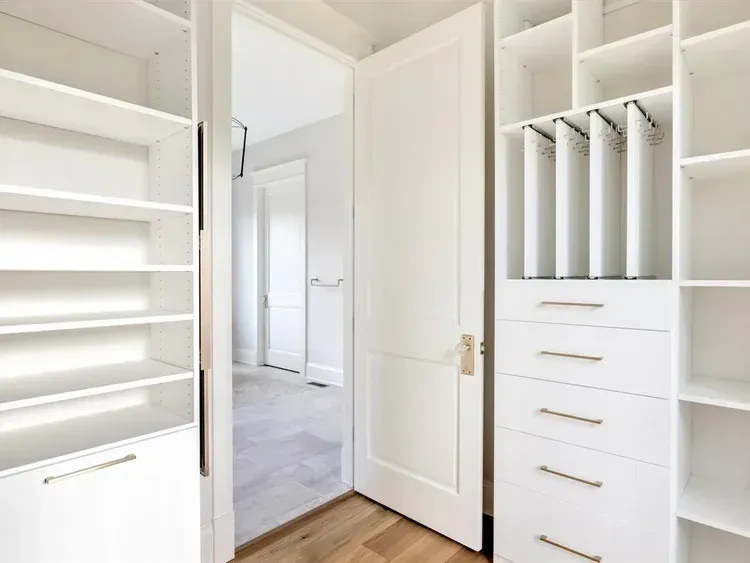 Bright white walk-in closet with shelves, drawers, and hanging space, viewed through open double doors.