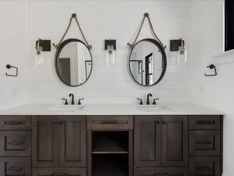 Modern bathroom double vanity with two round mirrors, wall sconces, and dark wood cabinets
