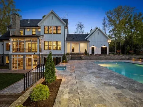 Luxury house with lit windows, pool, and stone patio at dusk