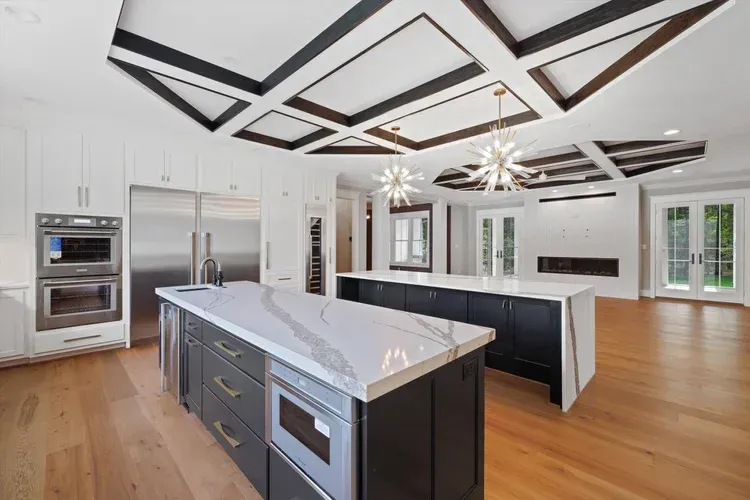 Modern luxury kitchen with white marble island, dark cabinets, hardwood floors, and geometric ceiling lights
