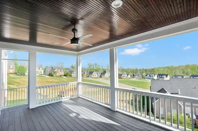 Covered front porch with white railing, dark ceiling fan, and a bright suburban neighborhood view.