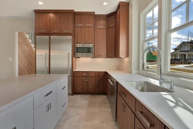 Modern kitchen with wood cabinets, white countertops, stainless appliances, and a large window over the sink