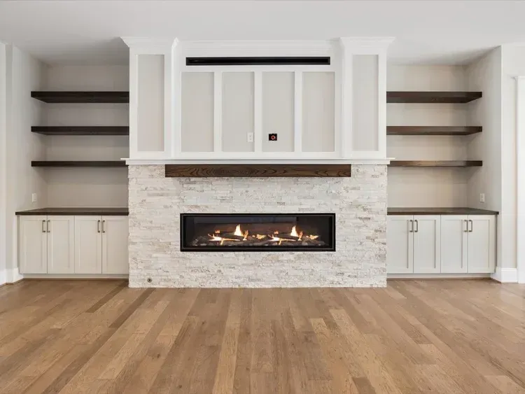 Modern living room with a white built-in fireplace, stone surround, dark shelves, and wood flooring