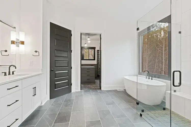 Modern bathroom with white vanity, freestanding tub, glass shower, and gray tile floor.