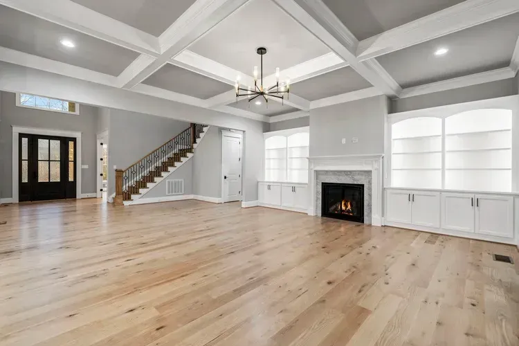 Bright empty living room with vaulted ceiling, fireplace, staircase, and light wood floors