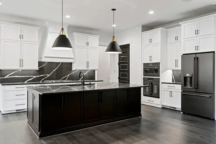 Modern kitchen with white cabinets, black island, stainless steel appliances, and pendant lights