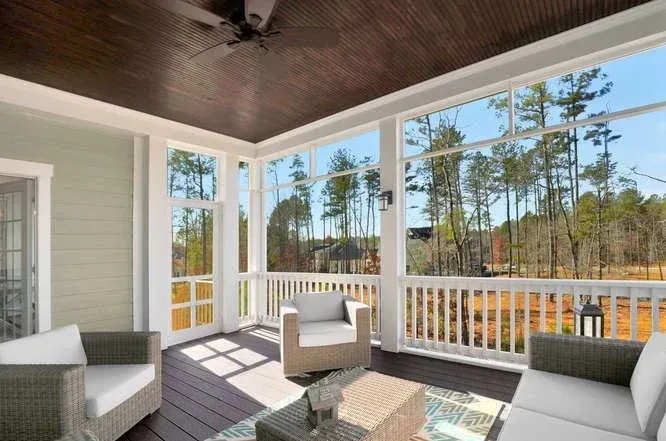Covered porch with white furniture, dark ceiling, and a view of trees through railing and windows