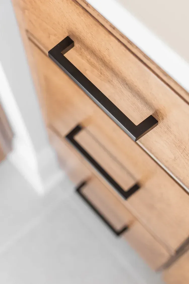 Three black handles on a light wood dresser drawer