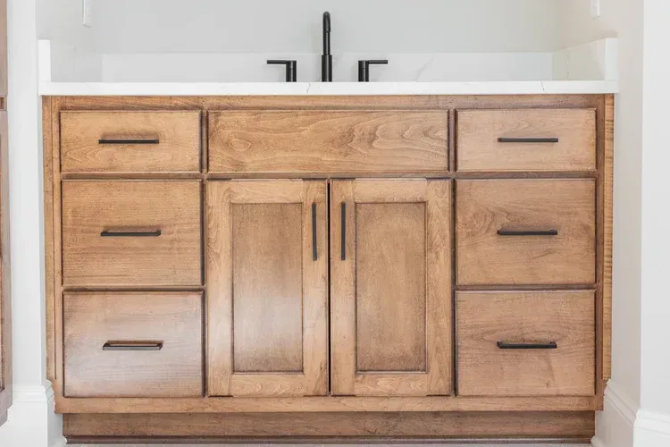 Wooden bathroom vanity with white countertop, black faucet, and multiple cabinet drawers and doors