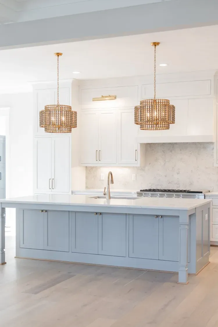 Bright modern kitchen with a pale blue island, white cabinets, and two woven pendant lights.