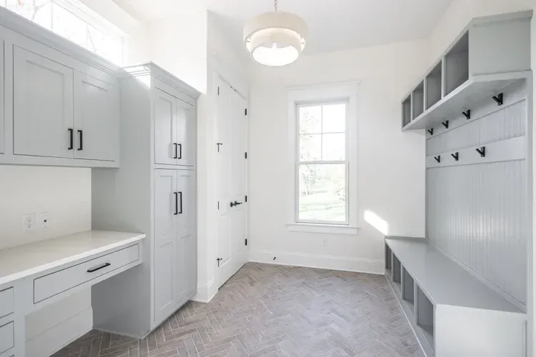 Bright white mudroom with built-in cabinets, bench, hooks, and a window.