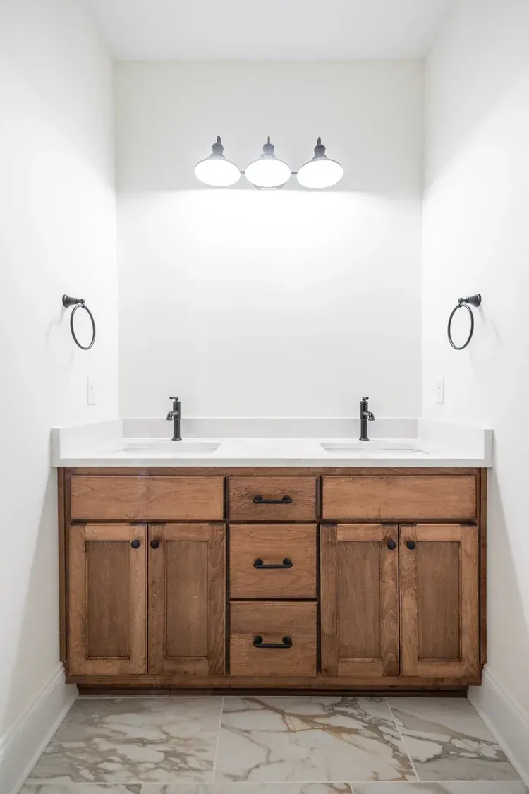 Small bathroom vanity with wood cabinets, white countertop, and three globe lights above a sink.