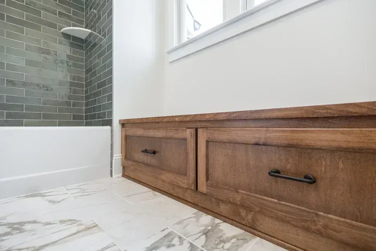 Wooden bathroom vanity with drawers beside a tiled shower and marble floor.
