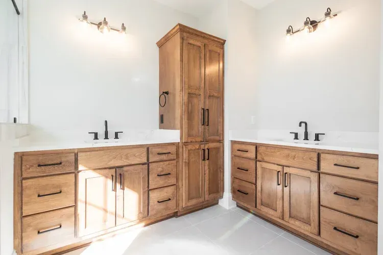 Bright bathroom vanity with wood cabinets, white countertops, double sinks, and tall center storage cabinet