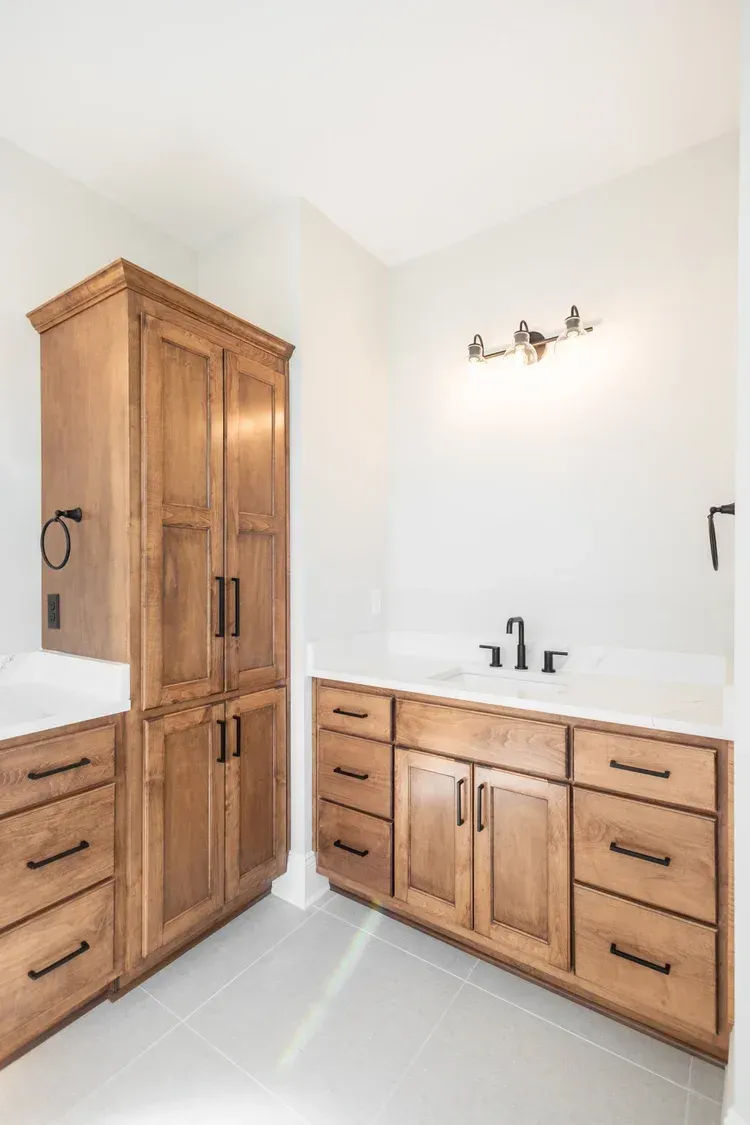 Bright bathroom with tall and low wooden cabinets, white walls, and a double sink vanity