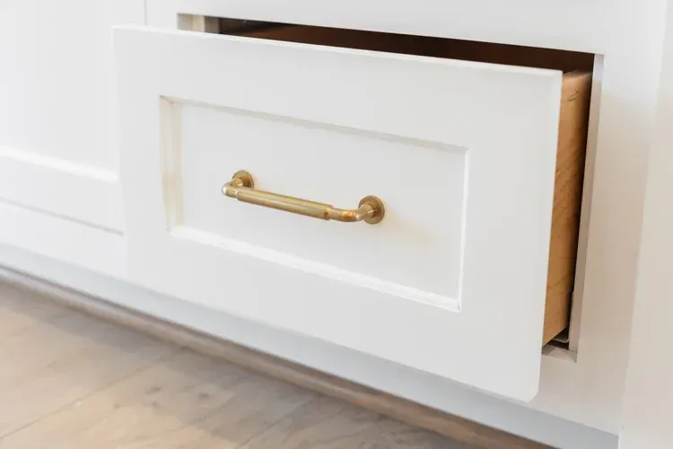 Partially open white cabinet drawer with a gold handle