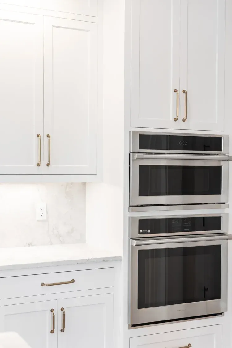 White kitchen cabinets with built-in stainless steel oven and microwave stack.