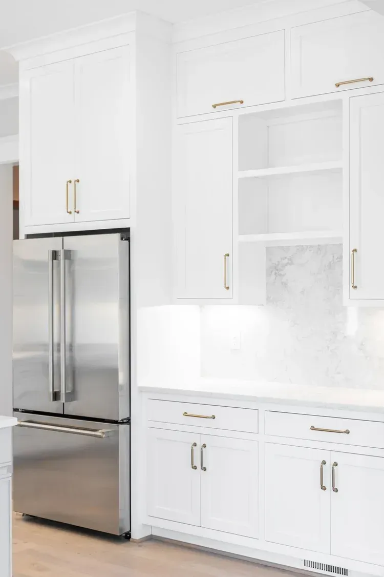Bright white kitchen with stainless steel refrigerator, cabinets, and marble backsplash.