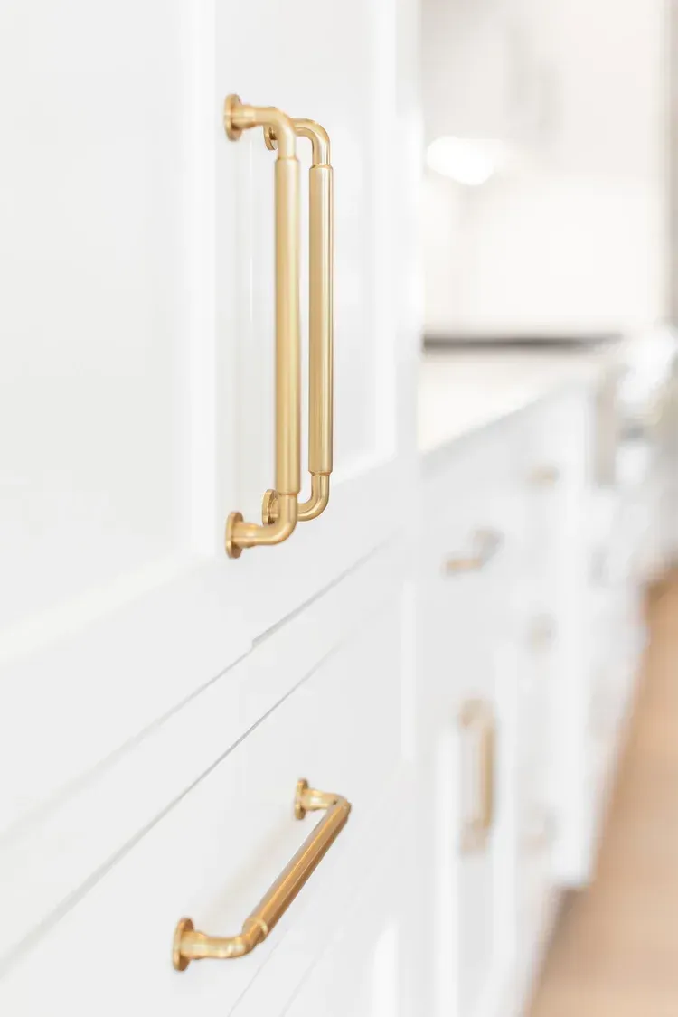 White kitchen cabinets with gold handles in a bright interior.