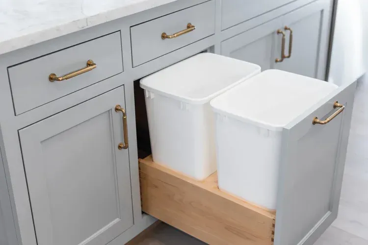 Kitchen cabinets with a pull-out wooden drawer holding two white trash bins