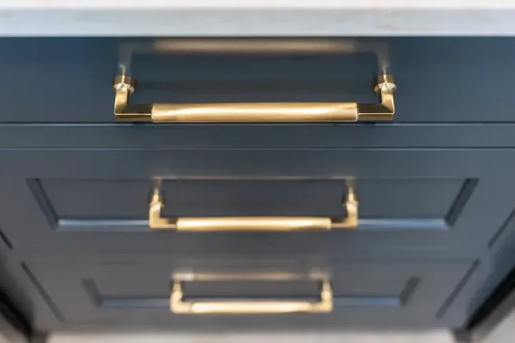 Close-up of dark blue cabinet drawers with gold bar handles