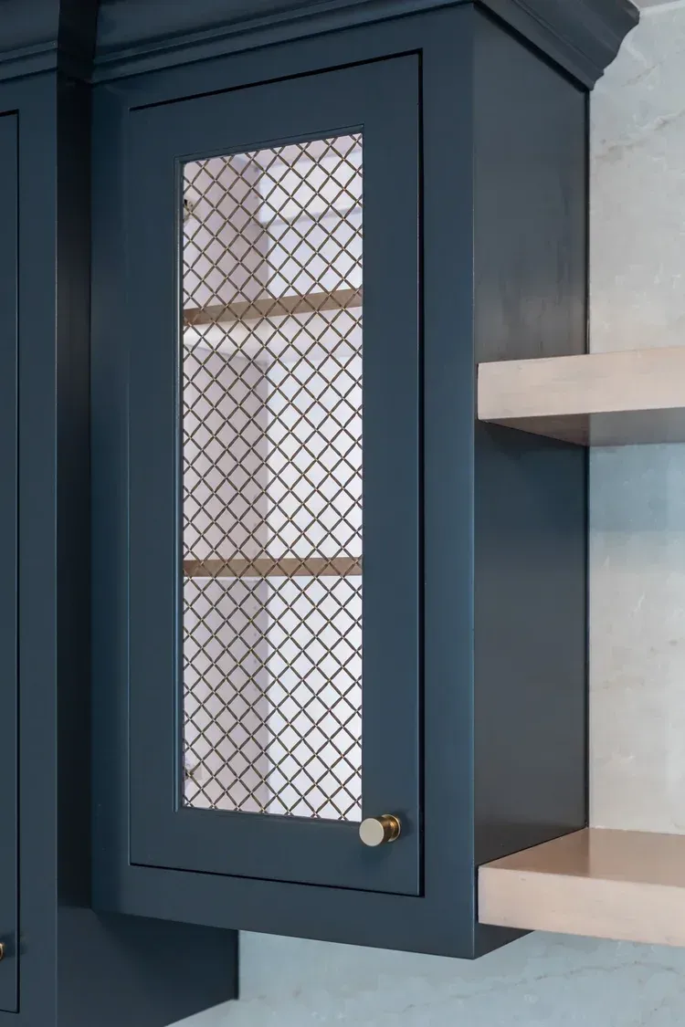 Dark blue kitchen cabinet with a wire-mesh glass door and brass knob, beside open shelving